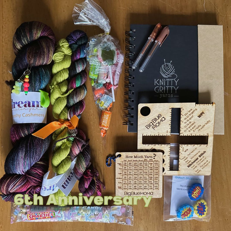 Collection of yarn, tools, and small items on a wooden surface with 'Knitty Gritty' branding.
