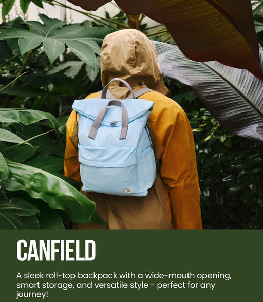 Person wearing a light blue backpack with green foliage in the background, featuring Canfield and Ori London branding.