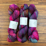Three skeins of multicolored yarn with labels on a wooden surface