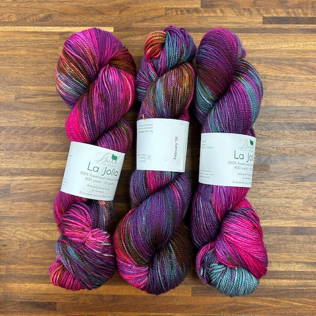 Three skeins of multicolored yarn with labels on a wooden surface