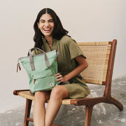 Woman holding a green bag sitting on a chair against a plain background