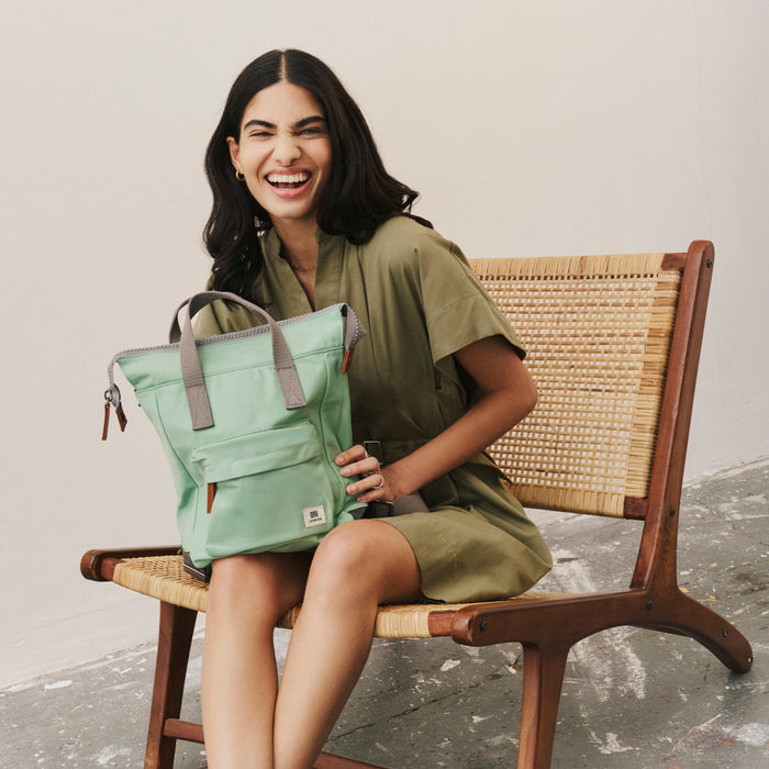Woman holding a green bag sitting on a chair against a plain background