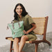 Woman holding a green bag sitting on a chair against a plain background
