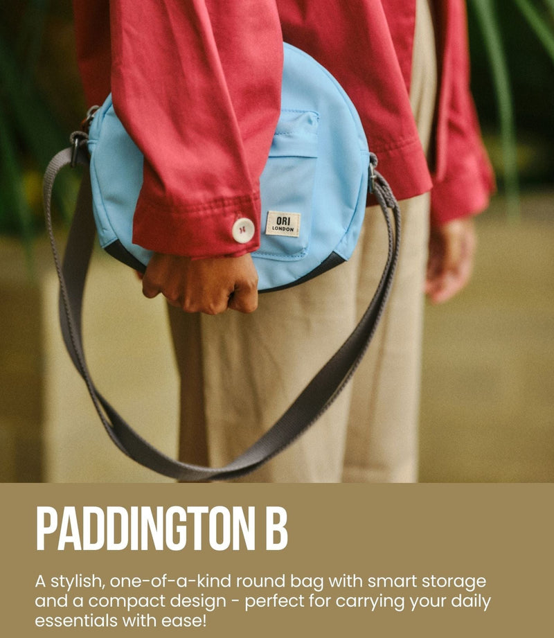 Person holding a blue round bag with 'Paddington B' branding, featuring the Ori London logo.