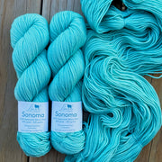 Two skeins of turquoise yarn with labels on a wooden surface