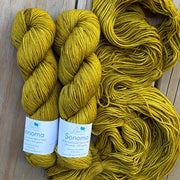 Two skeins of yellow yarn with labels on a wooden surface
