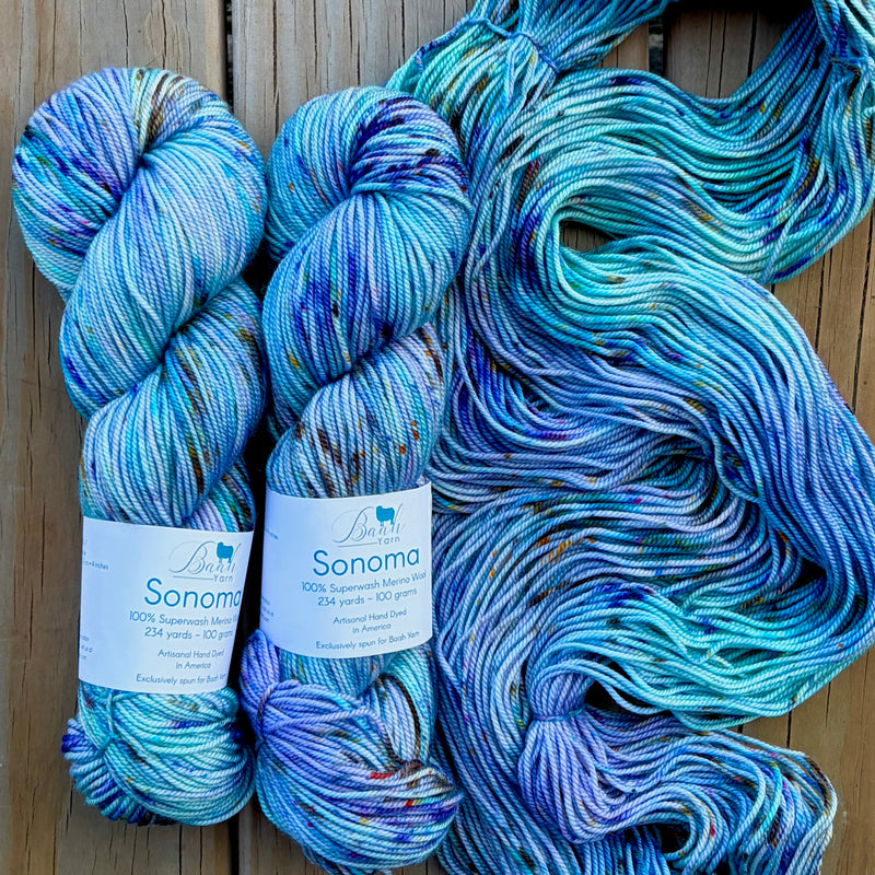 Blue and green yarn skeins with 'Sonoma' labels on a wooden surface