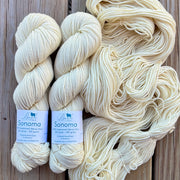 Two skeins of cream-colored yarn with labels on a wooden surface
