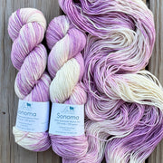 Three skeins of purple and white yarn with labels on a wooden surface