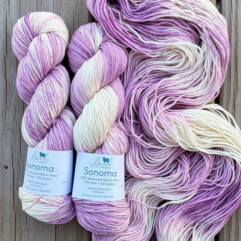 Three skeins of purple and white yarn with labels on a wooden surface