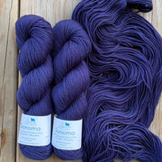 Two skeins of purple yarn with labels on a wooden surface