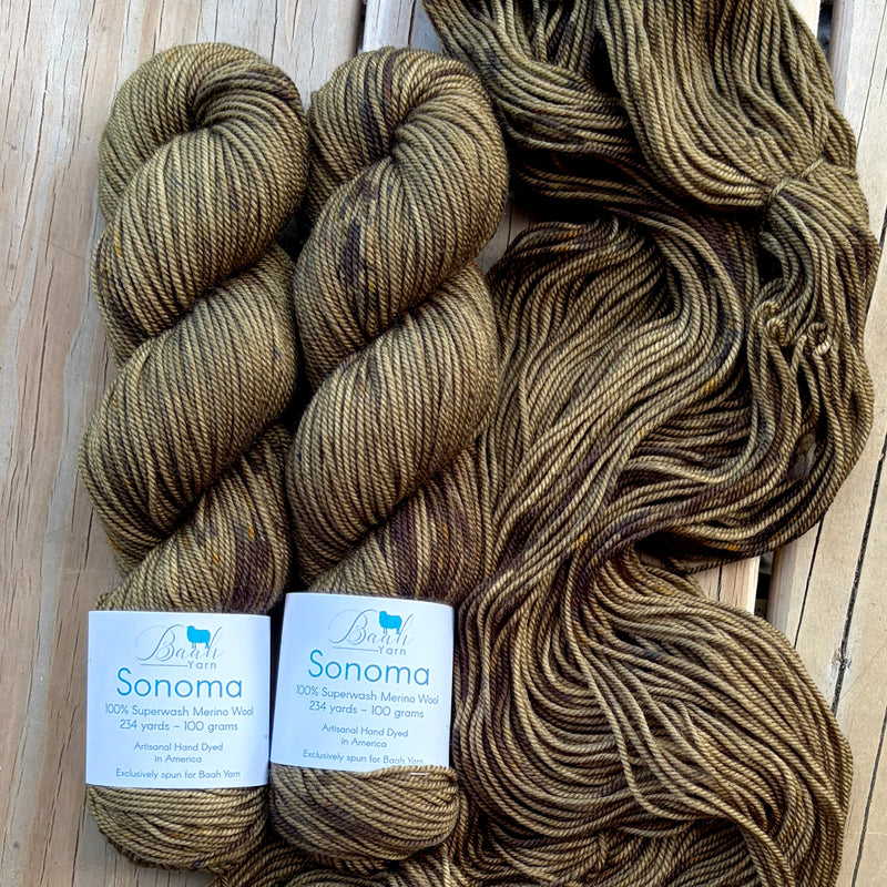 Three skeins of brown yarn with labels on a wooden surface