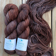 Two skeins of brown yarn with labels on a wooden surface