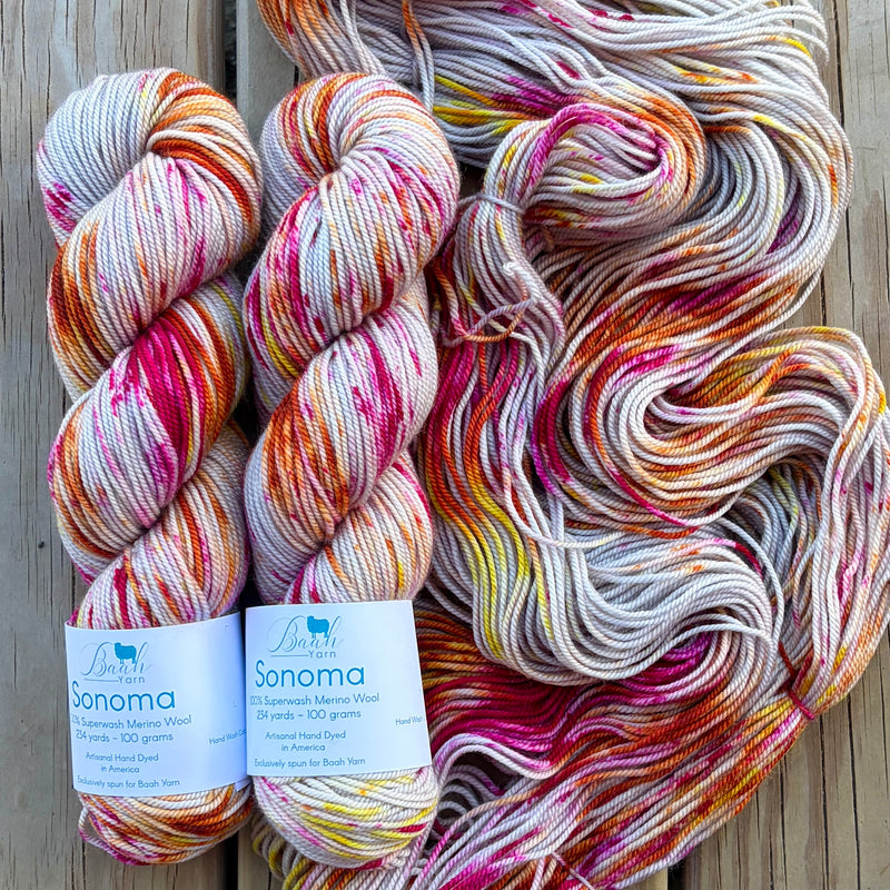 Three skeins of multicolored yarn with labels on a wooden surface