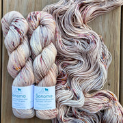 Two skeins of Sonoma yarn with a large skein behind them on a wooden background.
