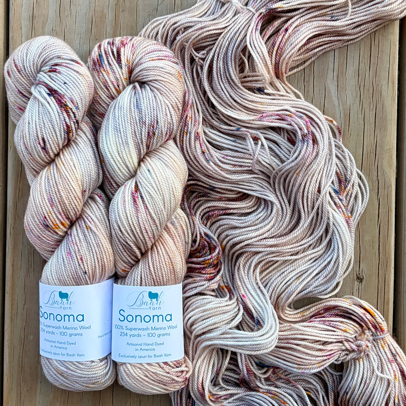 Two skeins of Sonoma yarn with a large skein behind them on a wooden background.