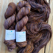 Three skeins of brown yarn with labels on a wooden surface