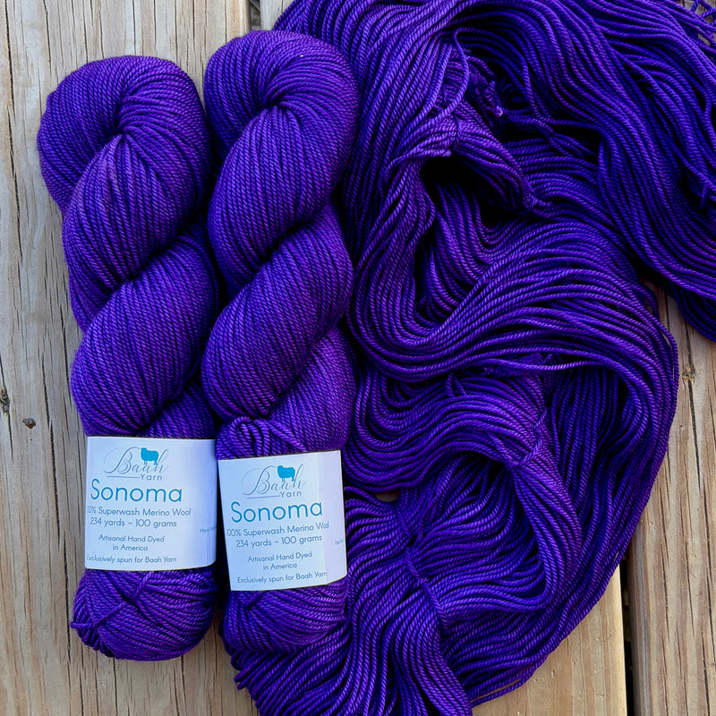 Two skeins of purple yarn with labels on a wooden surface