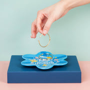 Blue floral-shaped dish with a hand placing a gold ring on it against a light blue background