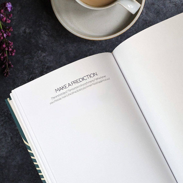 Open book with text on a dark surface with a cup and flowers.