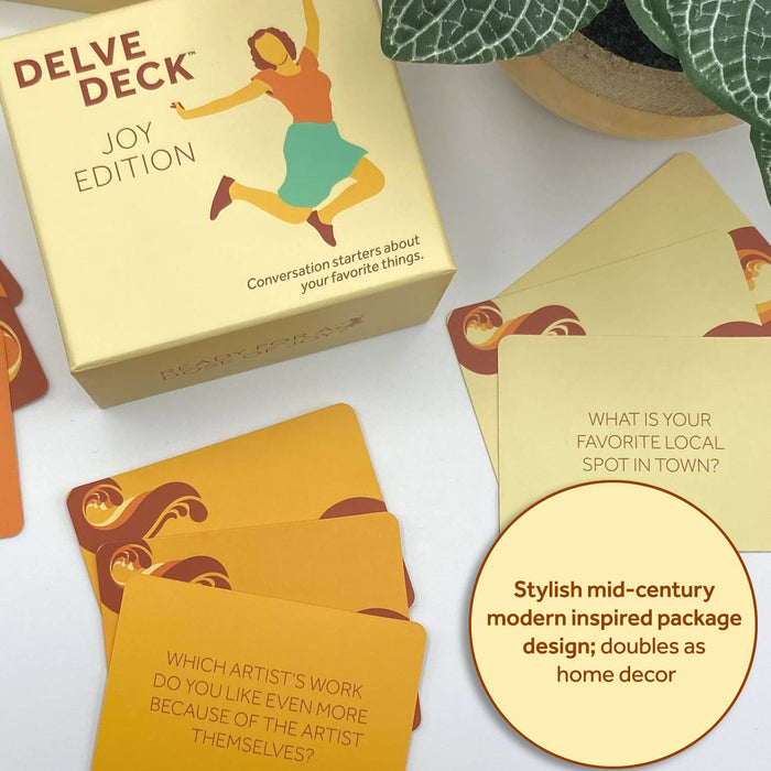 Delve Deck Joy Edition card game packaging and cards on a white surface with decorative elements.
