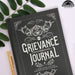 Grievance Journal book with decorative cover and gold pen on a light background
