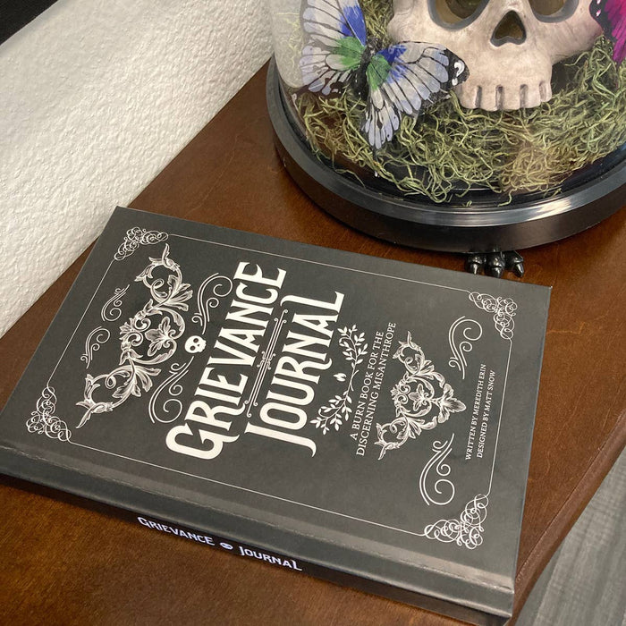 Grievance Journal book on a wooden surface with decorative skull and butterfly in the background