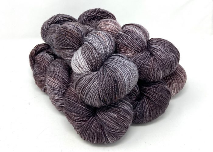 Three skeins of purple and gray yarn on a white background