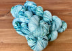Three skeins of blue and green yarn on a wooden surface