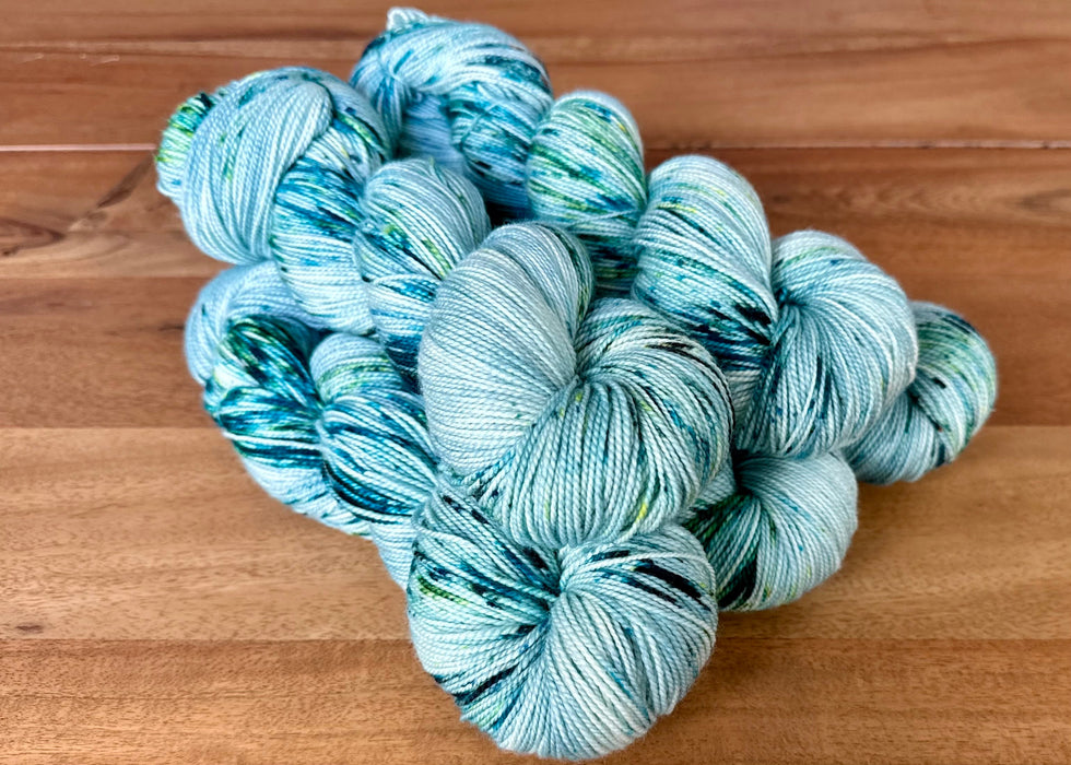 Three skeins of blue and green yarn on a wooden surface