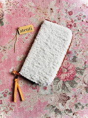White textured pouch with leather zipper pull on a floral pink background