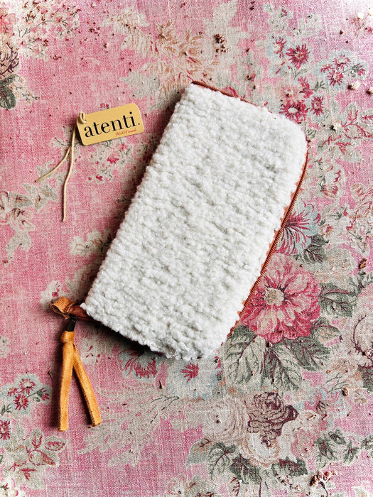 White textured pouch with leather zipper pull on a floral pink background