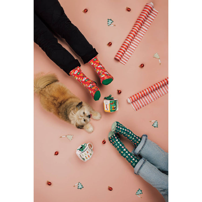 Two pairs of feet wearing colorful socks with a small dog and holiday-themed items on a pink surface.