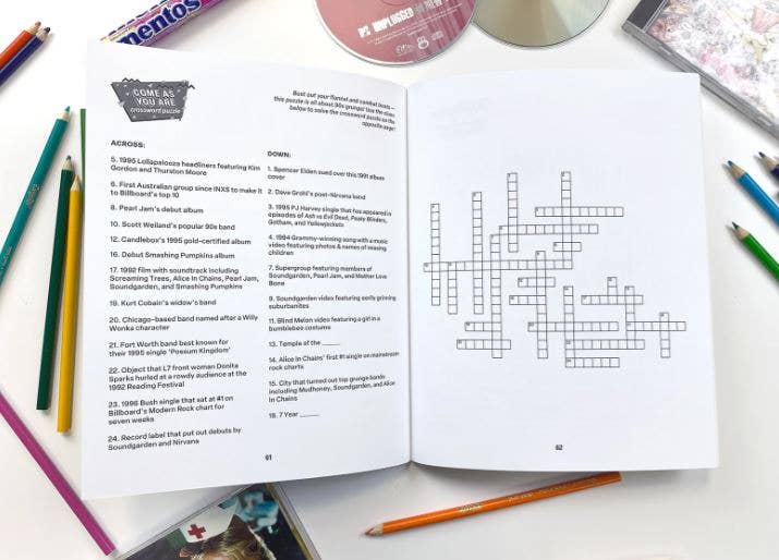 Open book with crossword puzzle and multiple colored pencils on a white surface
