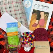 Yarn and knitting supplies with a 'Knitty Gritty' brand label on a red fabric background.